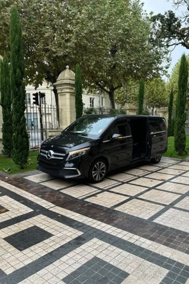 Van Mercedes noir stationné devant une façade en pierre.