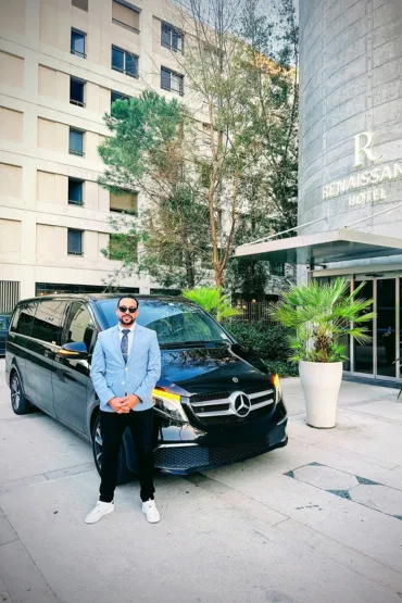 Chauffeur en costume bleu devant un van noir à l’entrée d’un hôtel.