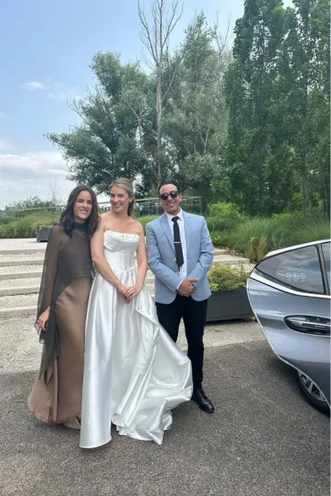 Mariée et deux accompagnantes posant avec un chauffeur près d’une berline.